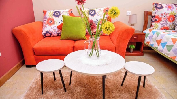 Ein Wohnzimmer mit einem roten Sofa, zwei weißen runden Tischen und einer Vase mit Blumen.