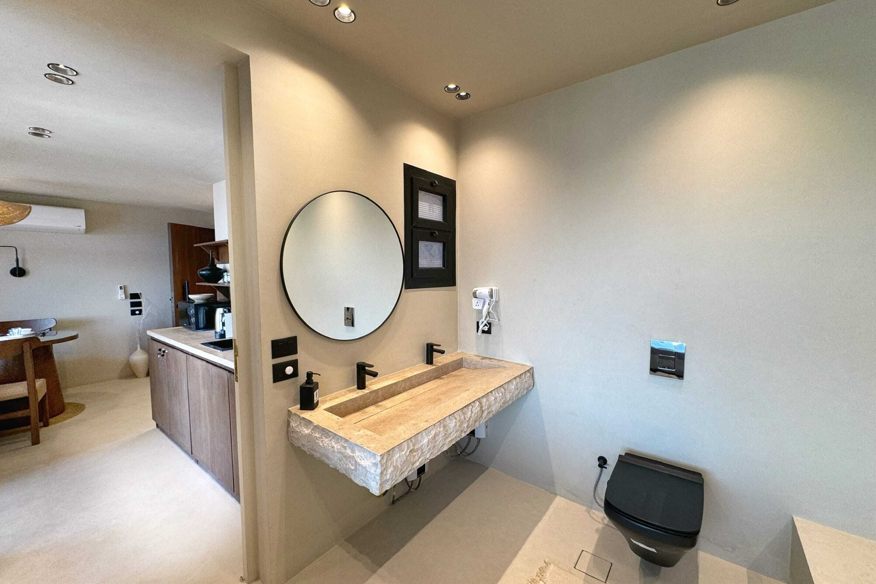 A modern bathroom with a large freestanding sink, a round mirror, and a toilet.