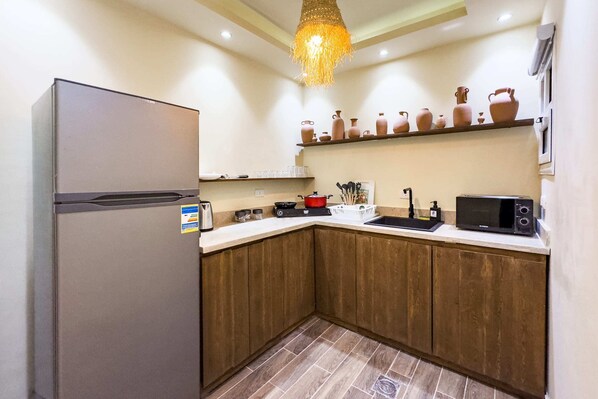 A kitchen with wooden cabinets, a refrigerator, a microwave, and a hanging light fixture. - Xuru Stays I The Pyramids Horizon Studio w/ Bathtub (Giza)