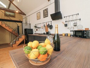 A kitchen with a wooden table, a fruit basket, a bottle of champagne, and a microwave. - The Old Workshop (Scarborough)