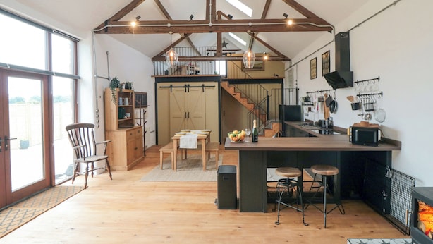 A spacious kitchen with wooden beams, a dining area, and a staircase leading to an upper level. - The Old Workshop (Scarborough)