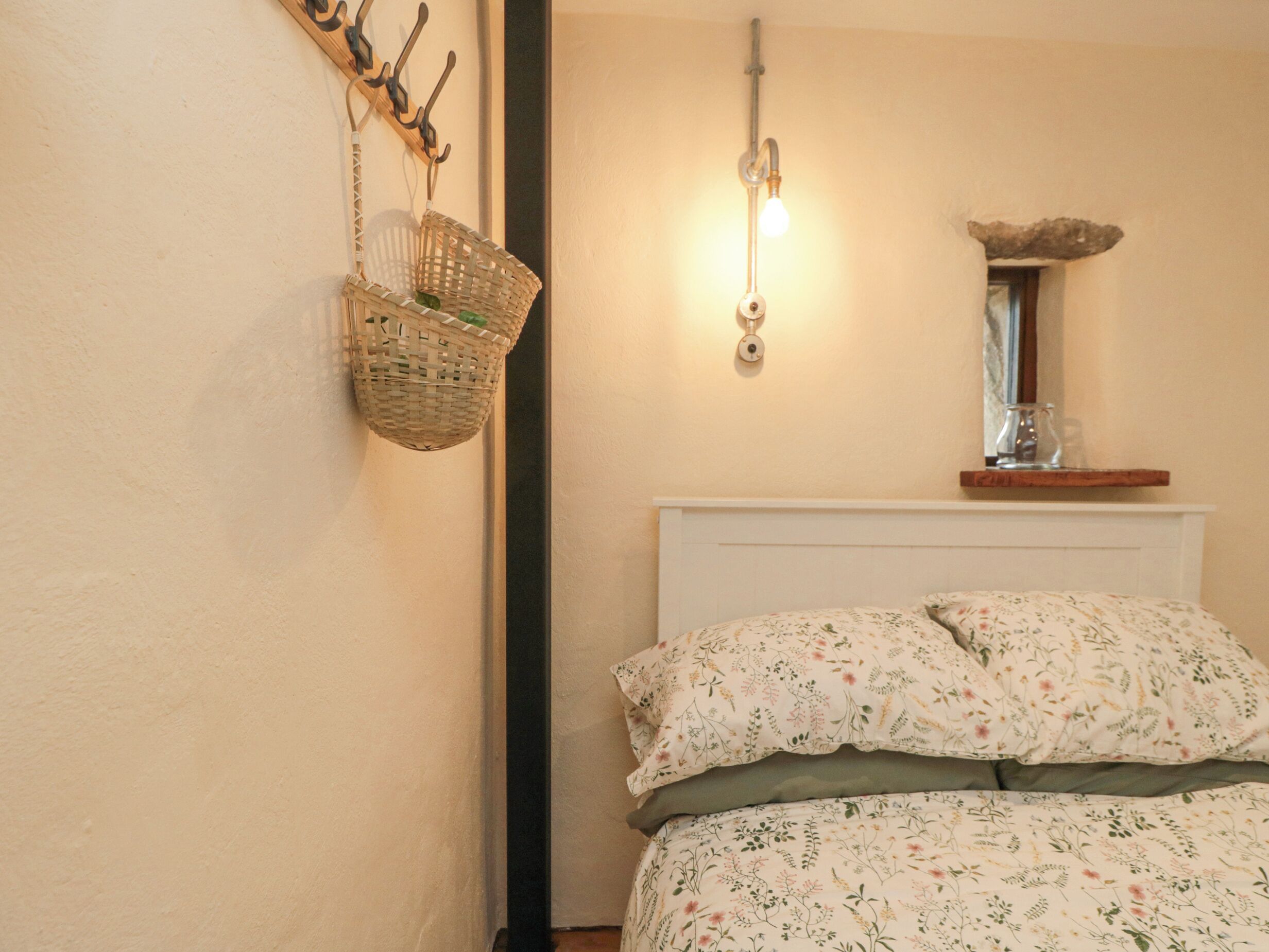 A bedroom with a bed, a wall-mounted light, a mirror, and a basket.
