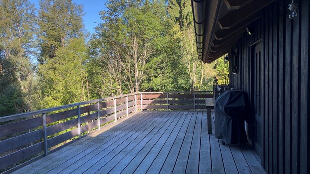 A wooden deck with a railing, a grill, and a building with a sloped roof. - Tobleralpe cozy self-catering hut in the Allgäu / Oberreute near Oberstaufen (Oberreute)