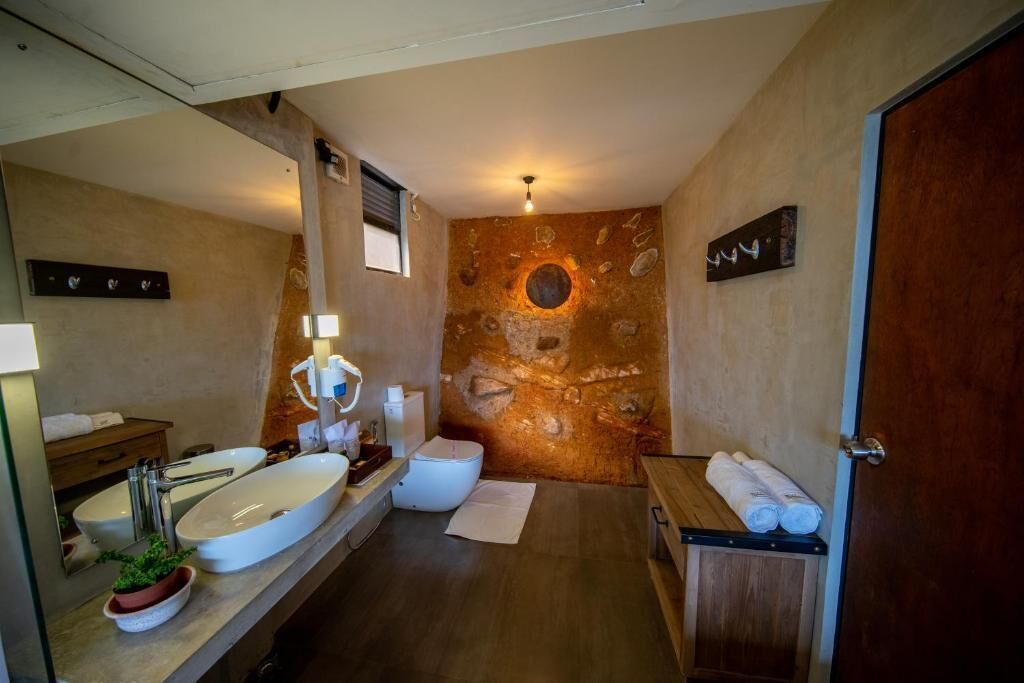 A bathroom with a large sink, toilet, and wooden bench.