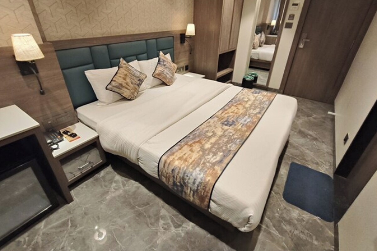 A neatly made bed with a patterned throw, a bedside table with a lamp, and a mirror reflecting the room.