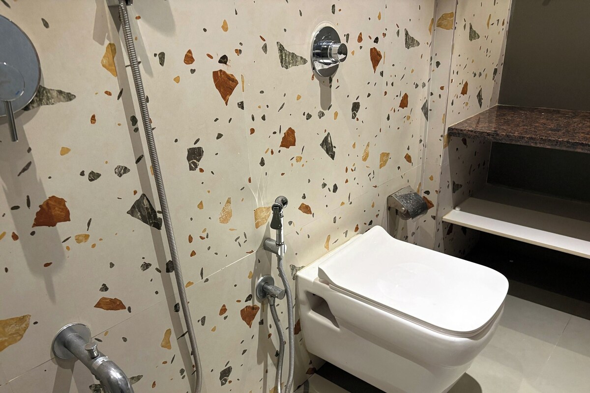 A bathroom with a white toilet, a shower with a metal hose, and a wall with a terrazzo finish.