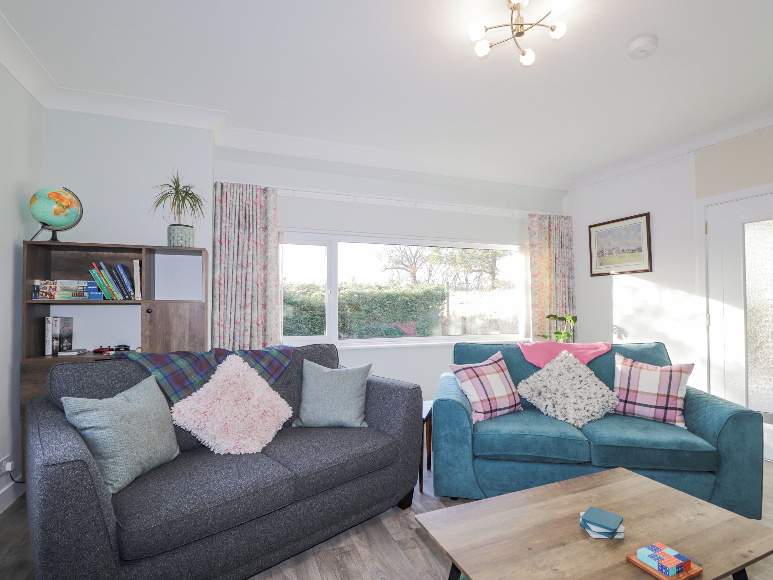 A living room with two sofas, a coffee table, a bookshelf, a globe, and a window with curtains.