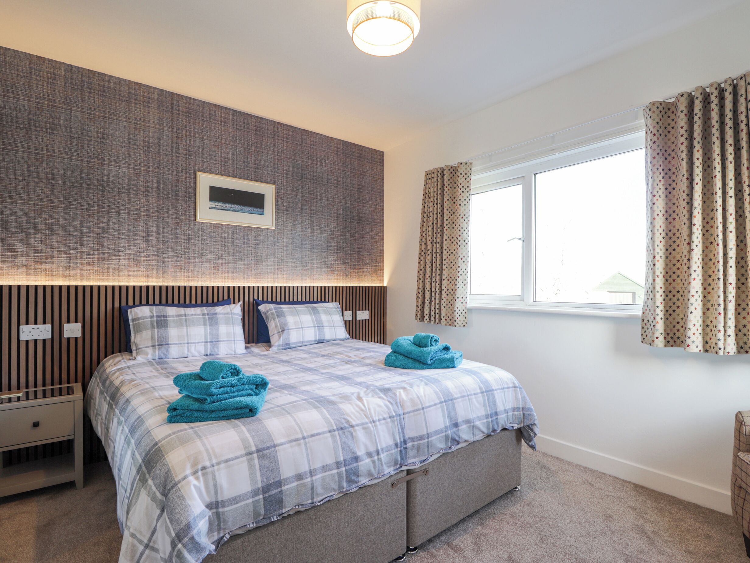 A bedroom with a bed, a nightstand, a wall-mounted TV, and a window with curtains.
