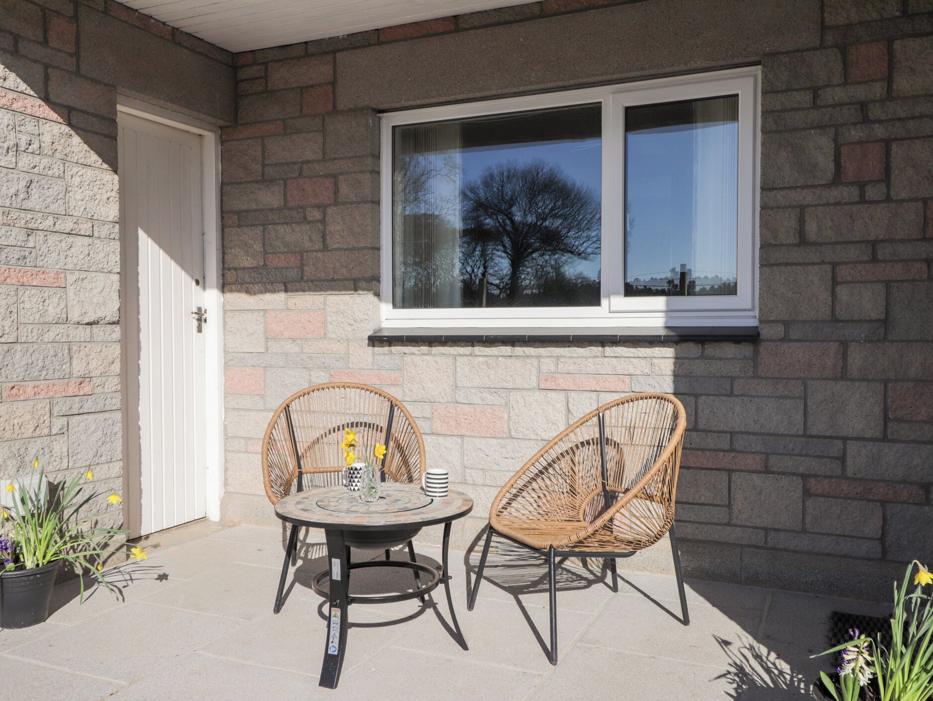 A patio with two wicker chairs and a table, a window, and a door.