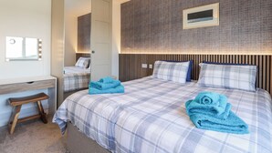 Habitación de hotel con una cama, un tocador con espejo e iluminación, un escritorio pequeño y un televisor montado en la pared.