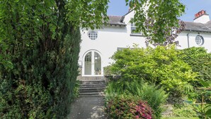 A pathway leading to a white house with a rounded door, surrounded by lush greenery and a stone wall. - Bron Y Graig (Conwy)