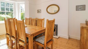 A dining room with a wooden table and chairs, a mirror on the wall, and a window with a view of greenery. - Bron Y Graig (Conwy)