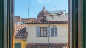Blick durch ein Fenster auf ein Gebäude mit einem Ziegeldach, einer Kuppel und einem Glockenturm.