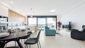 A modern living room with a dining area, a TV, and a balcony with a view. - CAMPORROSSO relax apartment (Finestrat)