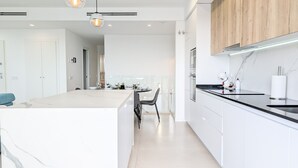 A modern kitchen with white cabinetry, a marble countertop, and a central island. There are two pendant lights above the island and a built-in oven on the right. - CAMPORROSSO relax apartment (Finestrat)