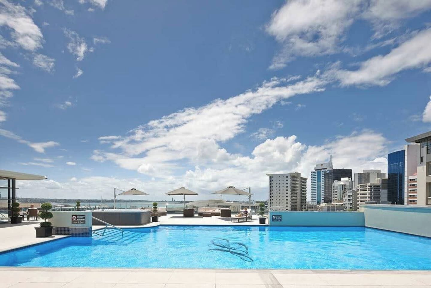 A rooftop pool with a city skyline view, lounge chairs, and umbrellas.