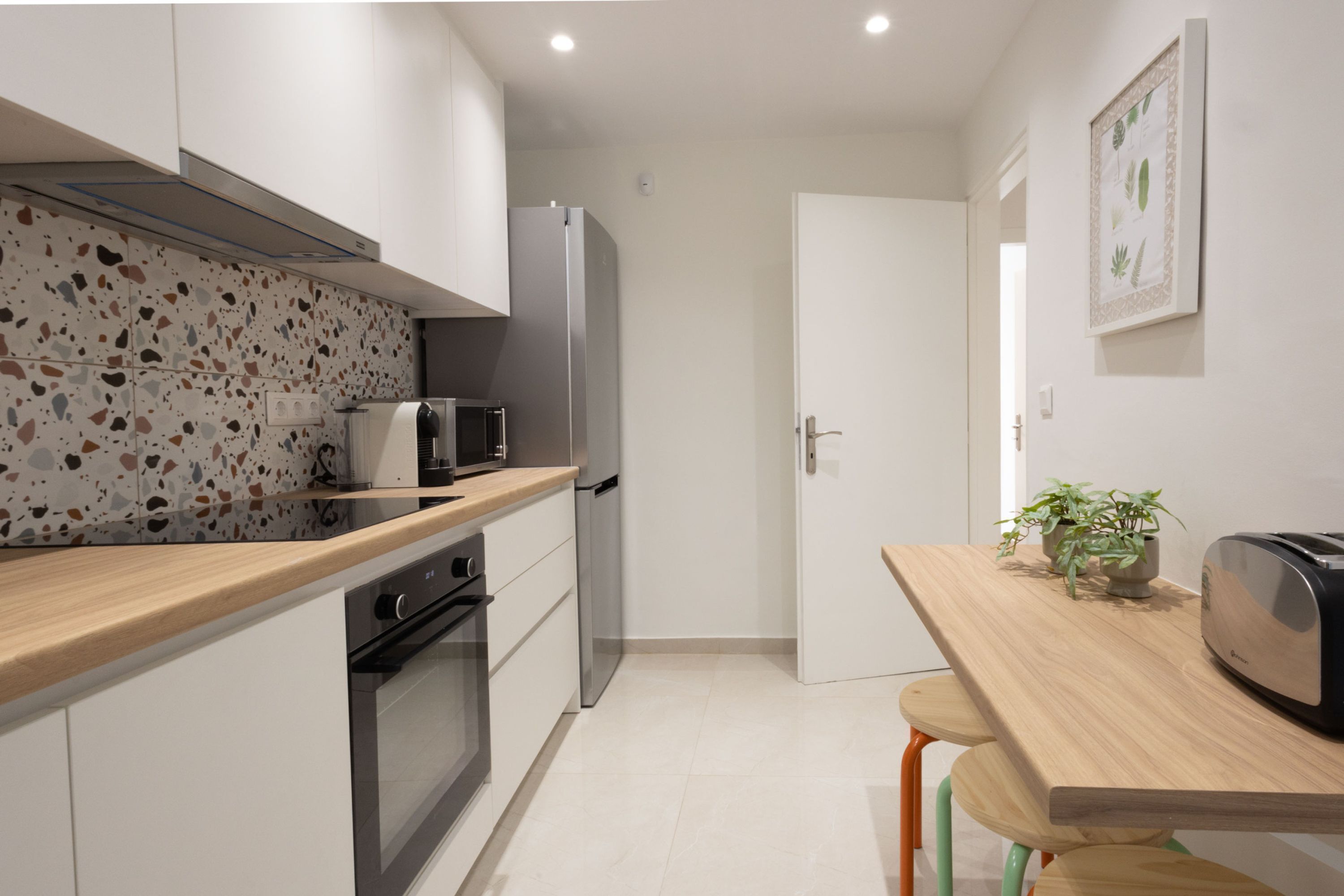 A compact kitchen with white cabinets, a microwave, a refrigerator, and a wooden countertop.