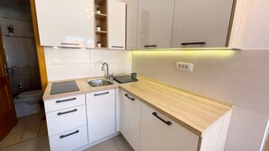 A modern kitchen with white cabinets, a wooden countertop, and a built-in shelf. - Apartman Kira 2 (Dramalj)