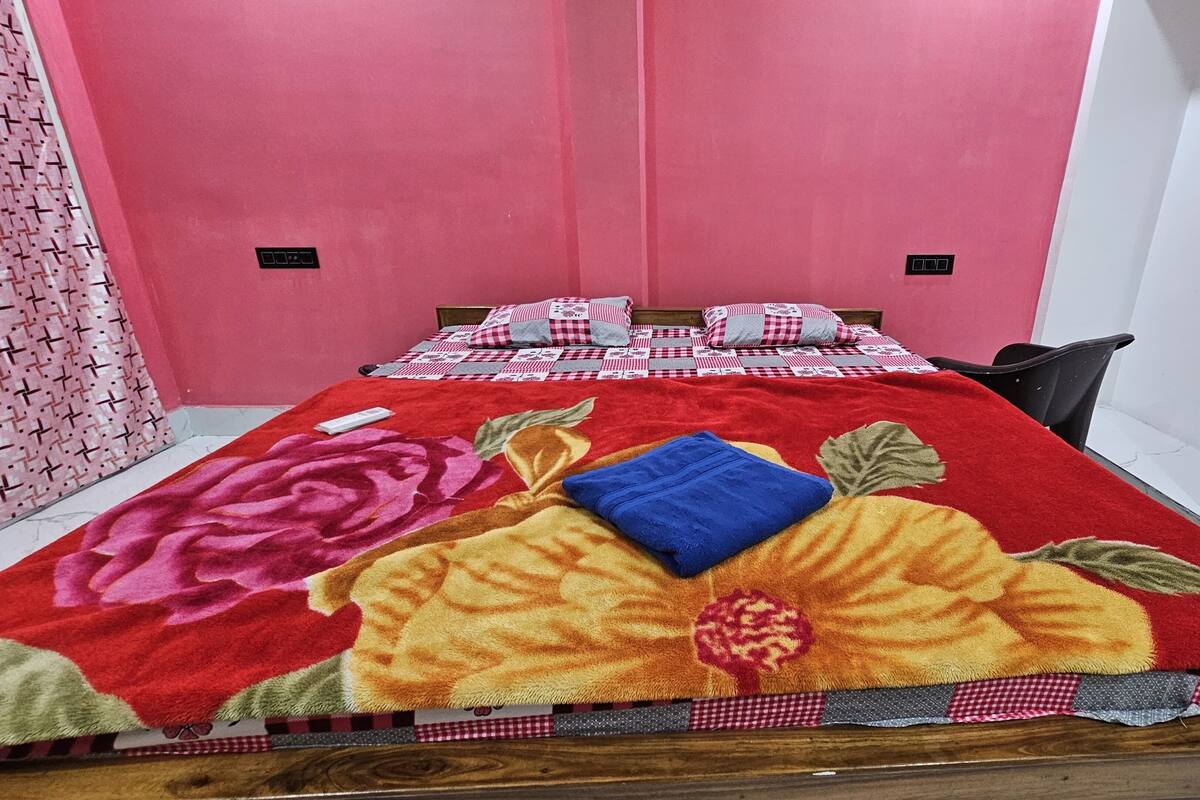 Una habitación con una cama cubierta por una colcha floral, un mantel a cuadros y una pared rosa.