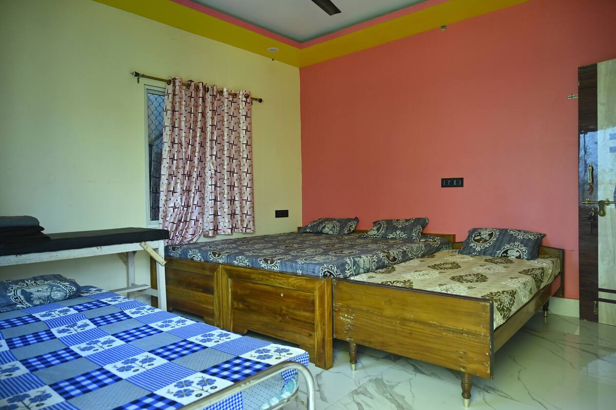 Un dormitorio con dos camas, cabecera de madera, ventana con cortina estampada y pared roja.