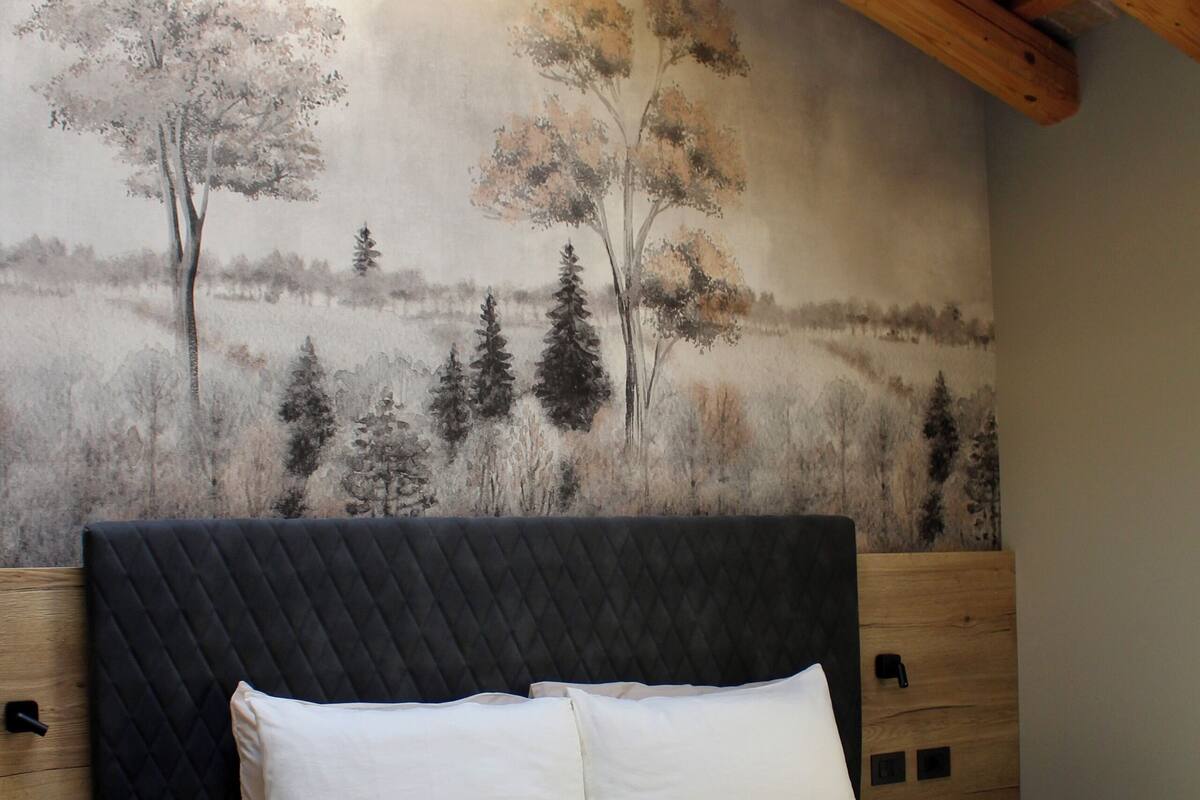 A bedroom with a large bed, a wooden headboard, a mural of trees on the wall, and a skylight above.