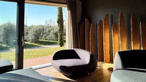 A modern living room with a large sliding glass door leading to an outdoor area, a round seating area, and a wooden accent wall. - Ida Boutique Hotel (Maser)