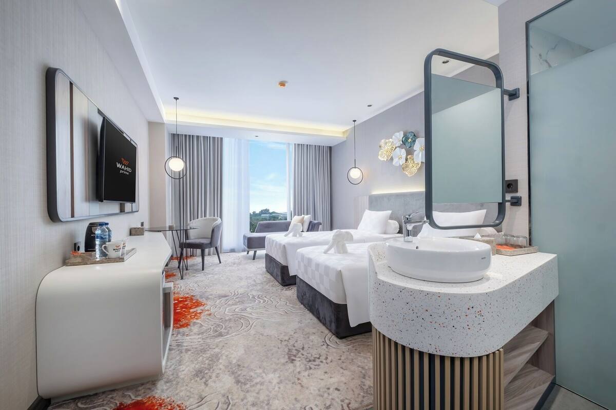 Moderni hotellihuone, jossa on suuri sänky, erillinen oleskelualue, suuri peili varustettu kylpyhuone ja seinälle asennettu televisio.