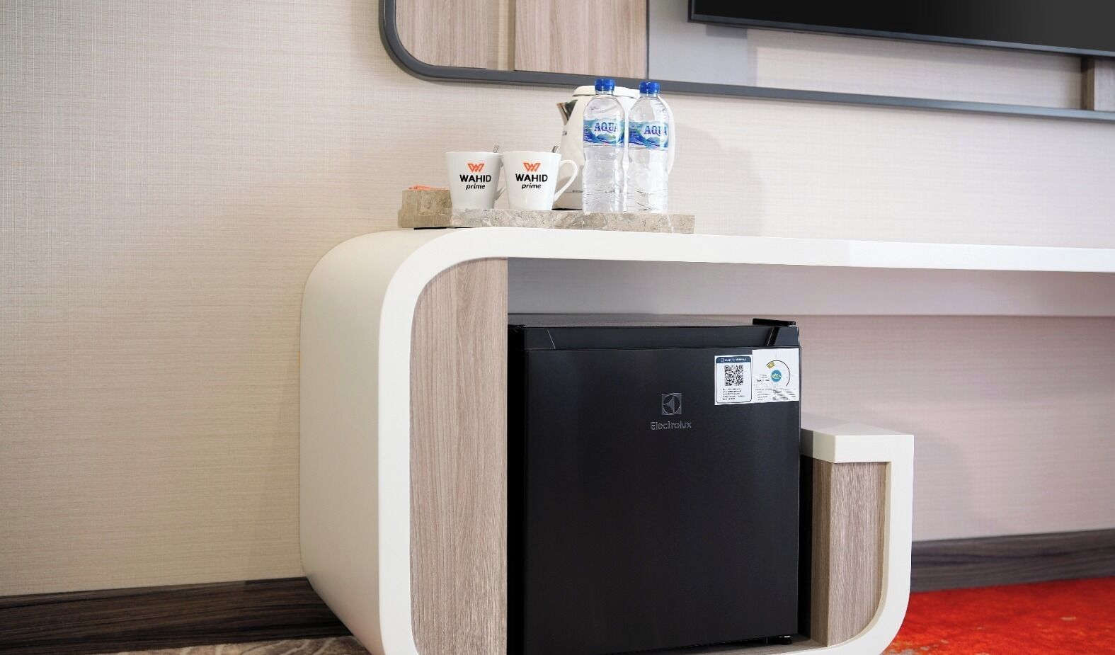 A modern hotel reception desk with a black refrigerator, two water bottles, and two branded coffee cups.