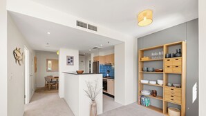 A modern kitchen with a central island, wooden shelving unit, and a dining area with chairs.