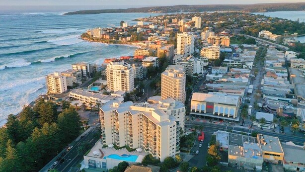 A coastal cityscape with high-rise buildings, a beach, and a road.