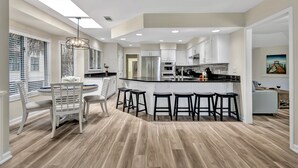 Una cocina moderna con una isla central, taburetes de bar y un comedor con mesa y sillas blancas.