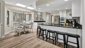 Una cocina moderna con una isla central, taburetes de bar y un comedor con sillas.