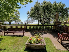 Un parc avec un banc, un parterre de fleurs et une statue.