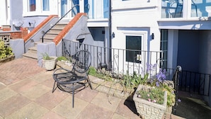 A townhouse with a patio, a black metal chair, a small garden, and a staircase. - Apt 2 @ Hunter's Quay (Bridlington)