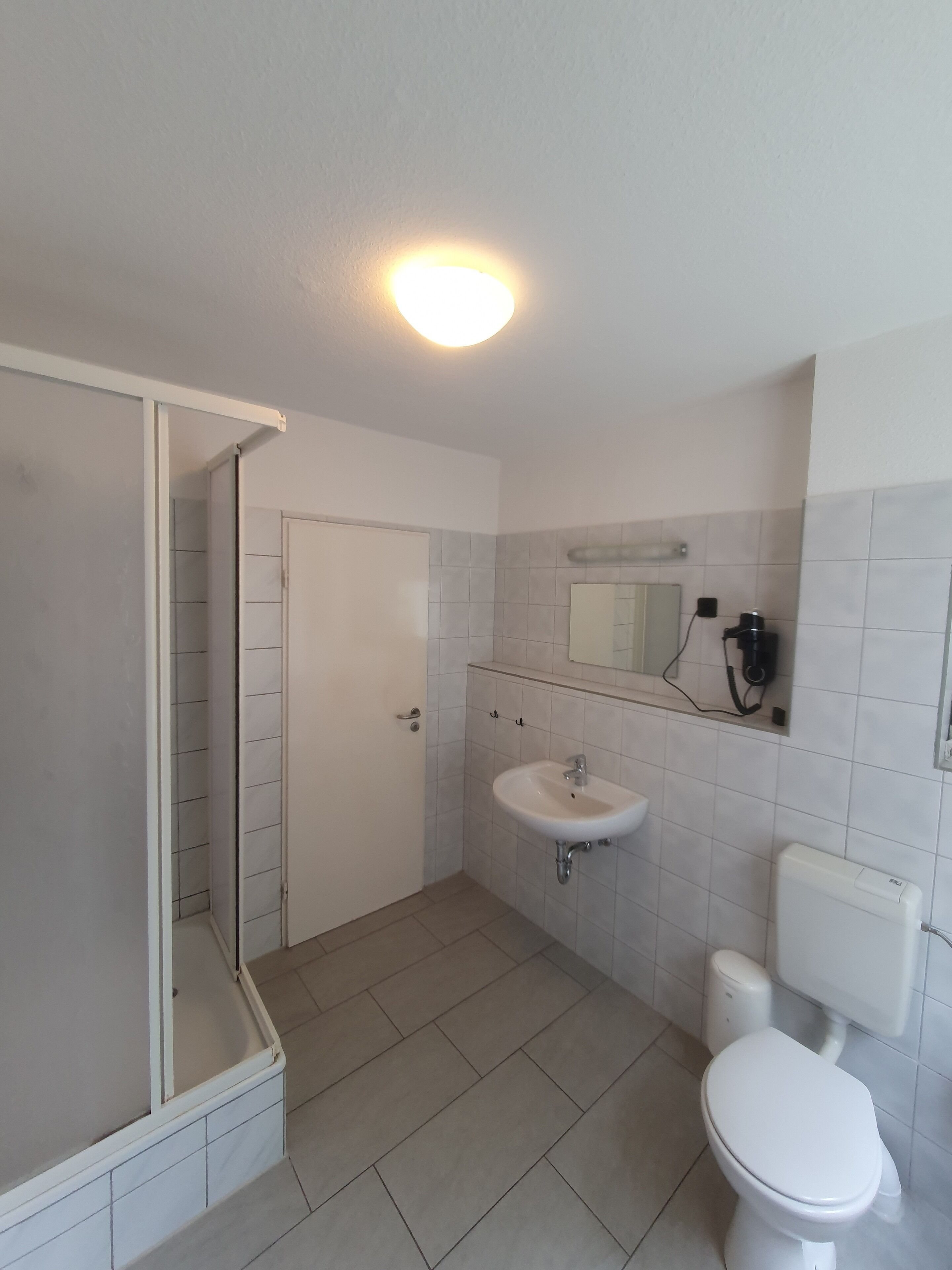 A bathroom with a shower, sink, toilet, and a mirror.