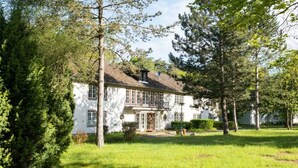 Een wit gebouw met een balkon, omringd door bomen en gras.
