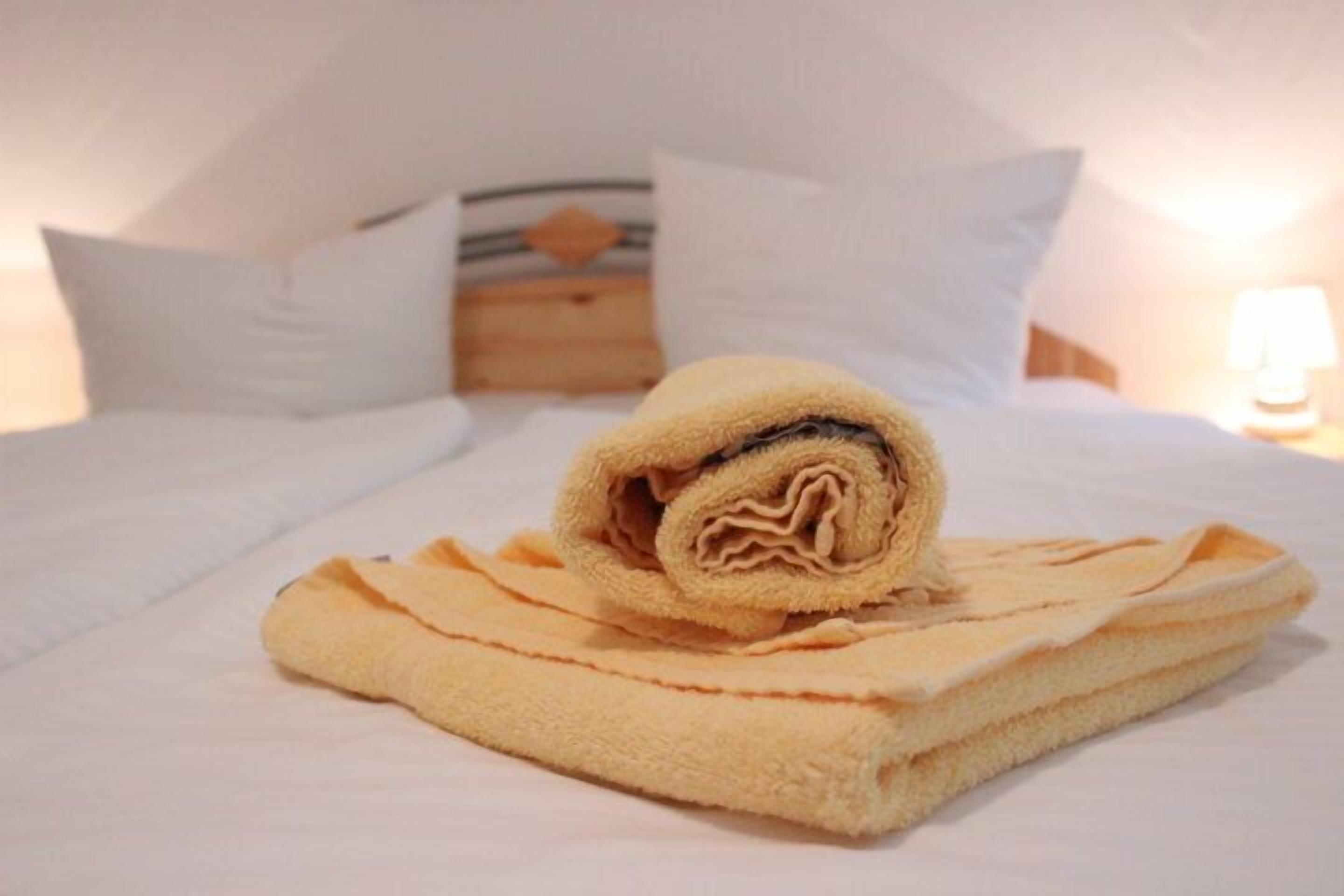 Una cama bien hecha con una toalla enrollada y una manta doblada sobre un edredón blanco.