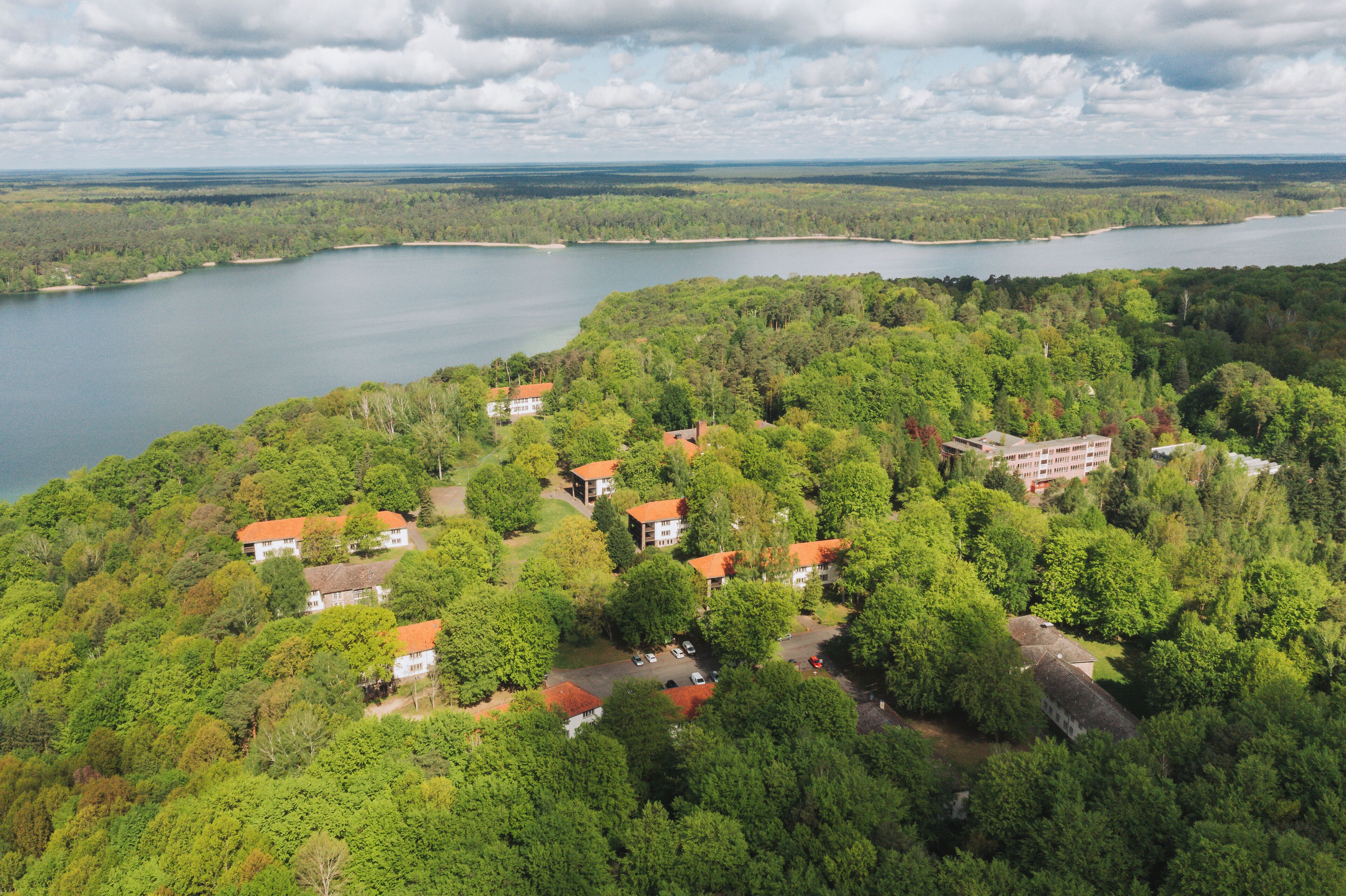 Vue aérienne d’une propriété au bord d’un lac, comprenant plusieurs bâtiments entourés d’une forêt dense.