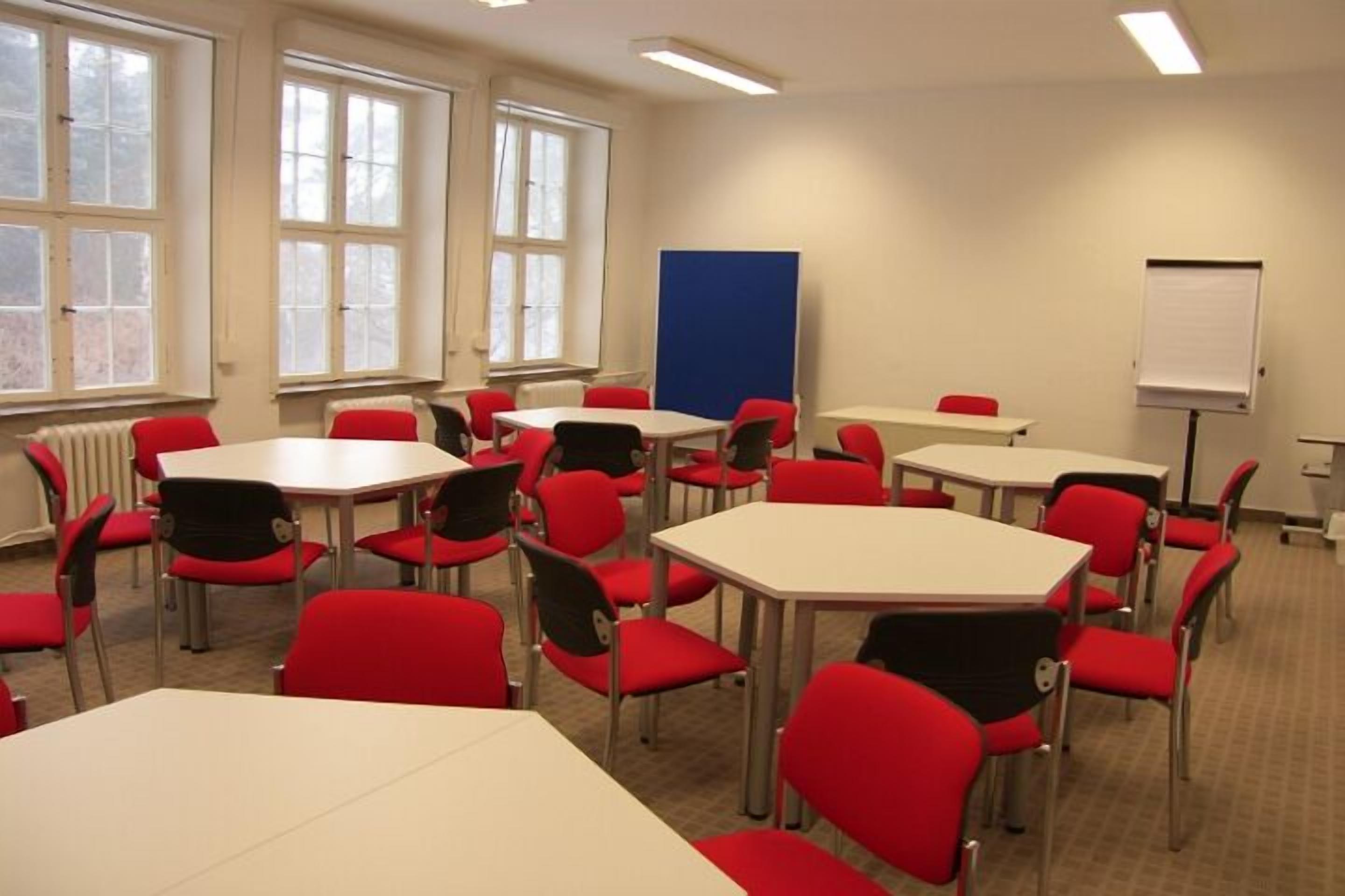 A conference room with multiple tables and red chairs, large windows, and a whiteboard.
