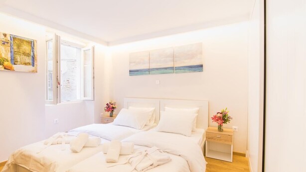 A double bed with white linens, a nightstand with a vase of flowers, and a painting of a seascape on the wall. - The Hidden Charm by Corfuescapes (Corfu)