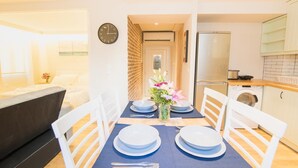 A dining area with a table set for four, a clock on the wall, and a kitchen in the background. - The Hidden Charm by Corfuescapes (Corfu)