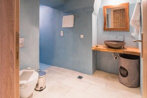A bathroom with a blue wall, a wooden vanity, a sink with a bowl, a toilet, a trash can labeled "laundry," and a towel hanging on a rack. - The Hidden Charm by Corfuescapes (Corfu)