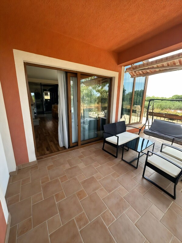 A patio area with a sliding glass door leading to an indoor space, a table with chairs, and a view of greenery outside.