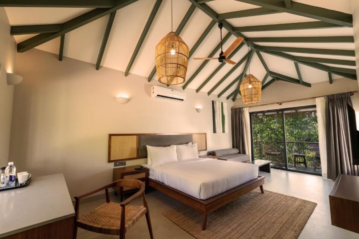 A bedroom with a bed, bedside table, chair, and a view of the outdoors.