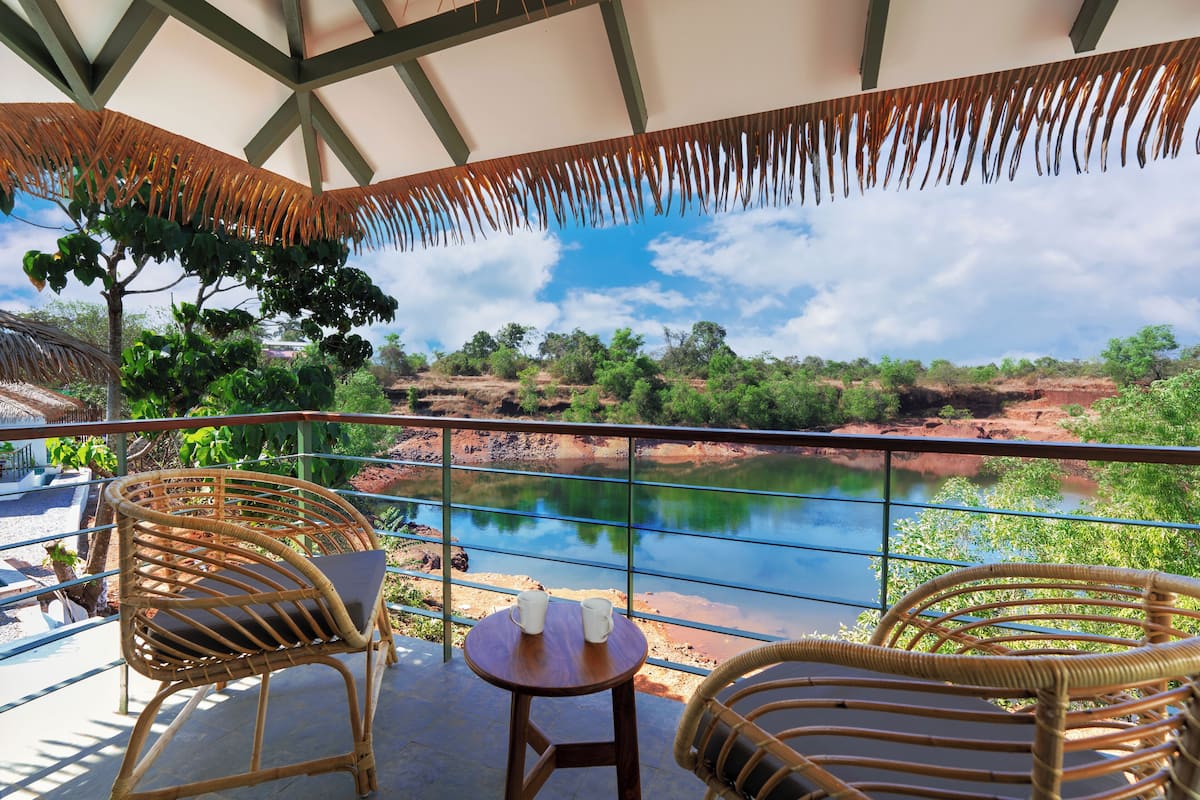A balcony with wicker chairs and a small table, overlooking a river and greenery.