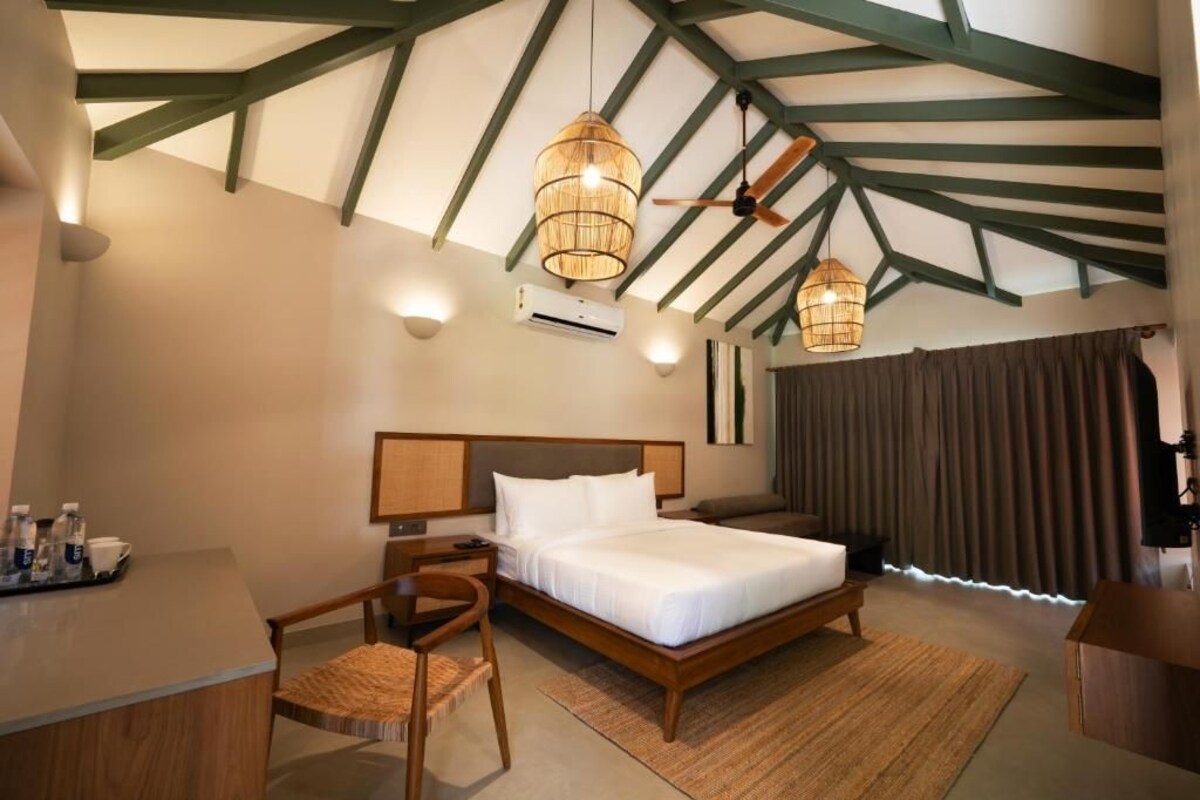 Quarto de hotel com cama, escrivaninha, cadeira e ventiladores de teto.