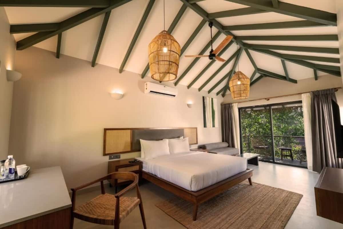 A bedroom with a bed, bedside table, chair, and a view of the outdoors.