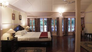 A spacious bedroom with a large bed, a nightstand with a lamp, and a view of the outdoors through large windows.