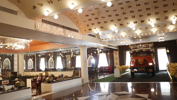 A hotel lobby with a central reception desk, a large mirror, and a red double-decker bus in the background.