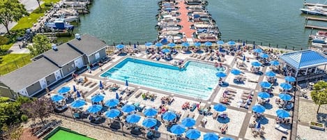 Enjoy a refreshing swim in our pool surrounded by sun loungers and umbrellas, with a dock and boats nearby.